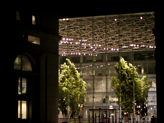 The atrium at the Thurgood Marshall Federal Judiciary Center in Washington, DC lit up inside at night shows trees and vegetation inside a large glass facade.